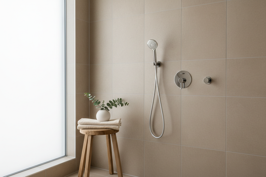 Minimalist bathroom interior with a chrome handheld shower head attached to a wall mount. Soft daylight, beige tiles, nordic spa style, clean and calm atmosphere. High-quality lifestyle photo.
